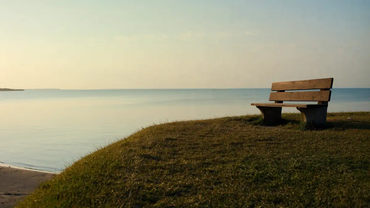 Calm Lake Michigan shore on a hazy July evening, with a wooden bench on a grass bluff in warm low light